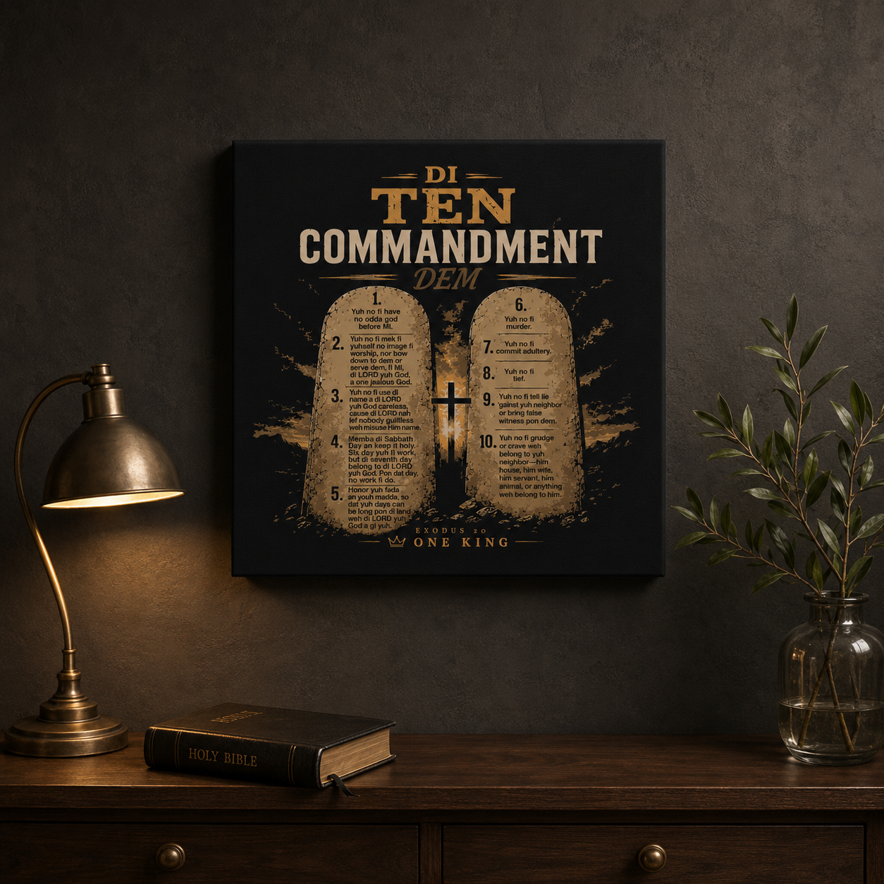 Black and gold Di Ten Commandment Dem Jamaican Patois Christian canvas displayed above a wooden console with a Bible, brass lamp, and greenery.
