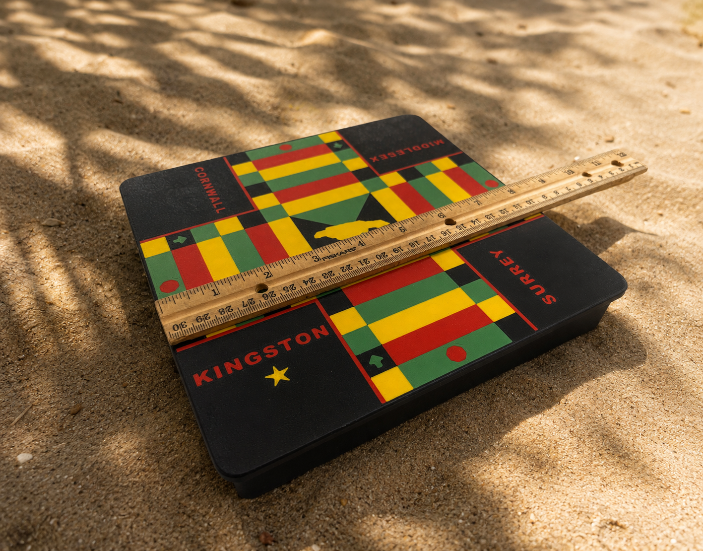 Colorful Kingston Surrey Cornwall middlesex 3d printed lock pon stop ludi board with Jamaican counties on sand with a ruler for scale