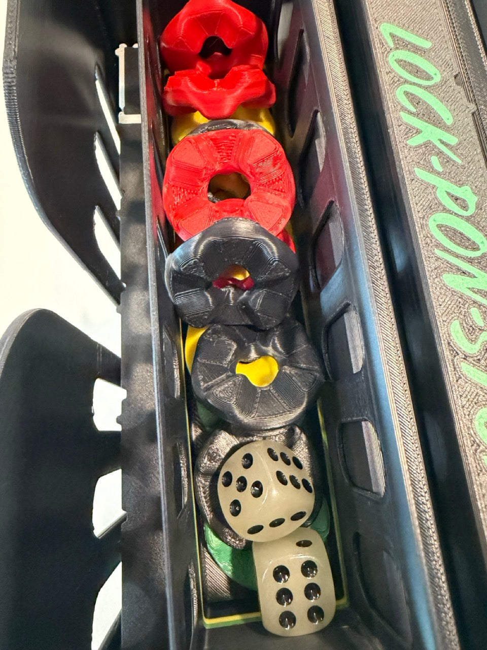 Game pieces and two dice stored inside the built-in compartment of the 24-inch non-magnetic Lock Pon Stop Jamaican Ludi board.