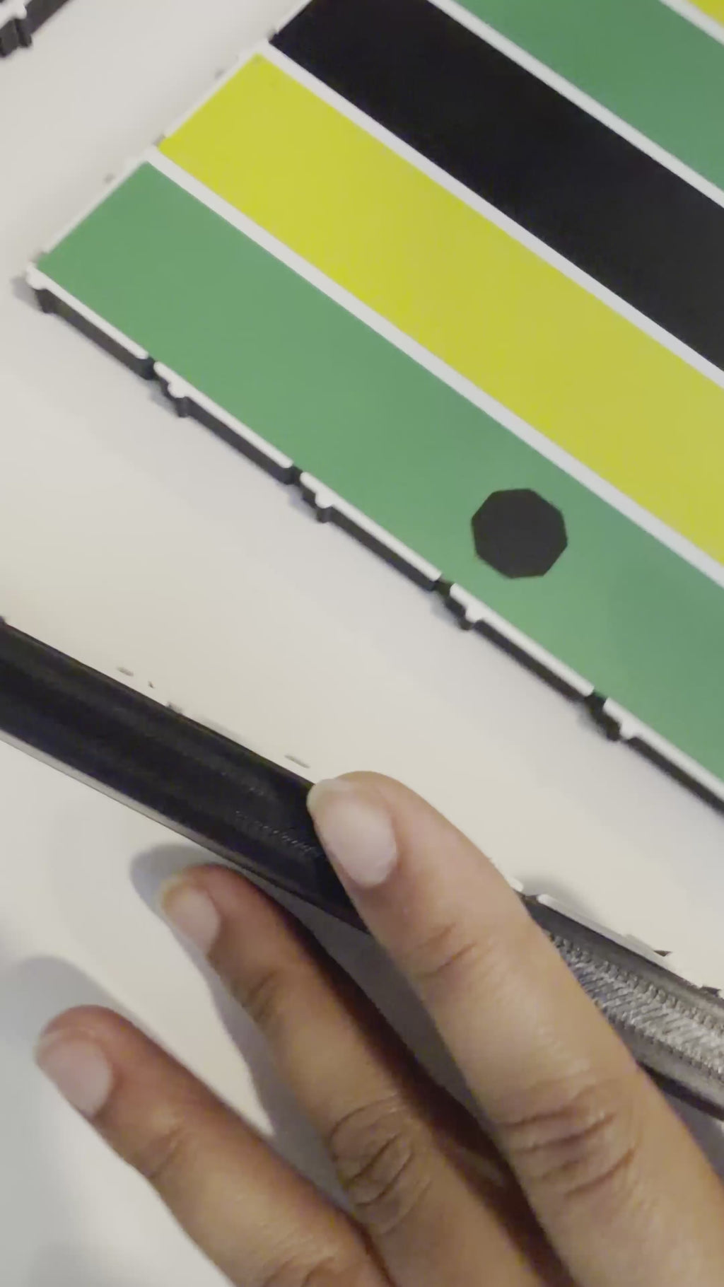Close-up video of hands assembling a premium 24x24-inch modular magnetic Jamaican Ludi board by attaching a border piece with built-in magnets. The snap-together design demonstrates quick setup and durable construction.